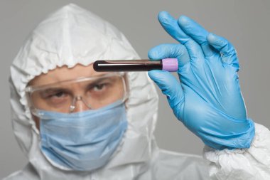 Scientific virologist. Biologist in protective suit and blue gloves holds test tube with blood. Test tube with viruses concept. Virus University employee.
