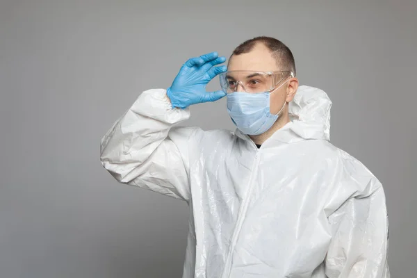 Scientific virologist. Biologist in protective suit and blue gloves puts on goggles. Viruses concept. Virus University employee.
