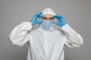 Scientific virologist. Biologist in protective suit and blue gloves puts on goggles. Viruses concept. Virus University employee.