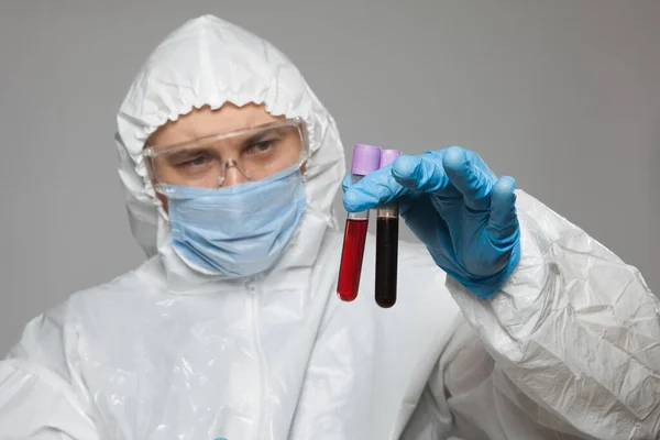 Scientific virologist. Biologist in protective suit and blue gloves holds test tubes with blood. Test tube with viruses concept. Virus University employee.
