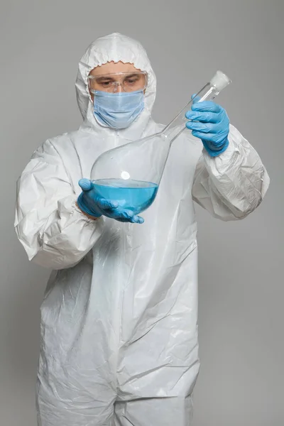 Scientific virologist. Biologist in protective suit and blue gloves holds big flask with blue substance sample. Flask with viruses concept. Virus University employee.