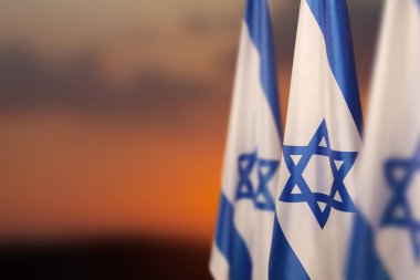 Israel flags with a star of David over cloudy sky background on sunset. Patriotic concept about Israel with national state symbols. Banner with place for text.