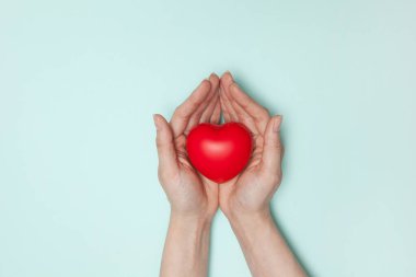 Sağlık, ilaç ve yardım konsepti. Küçük kırmızı kalpli kadınların ellerini kapatın. Düz yatıyordu.