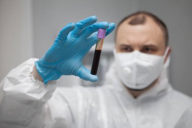 Scientific virologist. Biologist in protective suit and blue gloves holds test tube with blood. Test tube with viruses concept. Virus University employee.