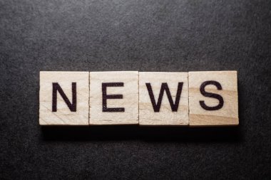 NEWS letter on wood block cubes on black background. Business communication concept.