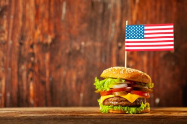 Close-up home made beef burger with american flag on the top on wooden table over old wooden background.