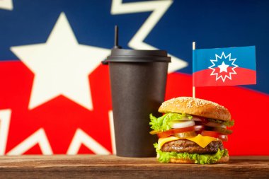 Classic American burger with juneteenth flag on the top and black paper cup with straw over juneteenth symbol background. Close-up with selective focus.