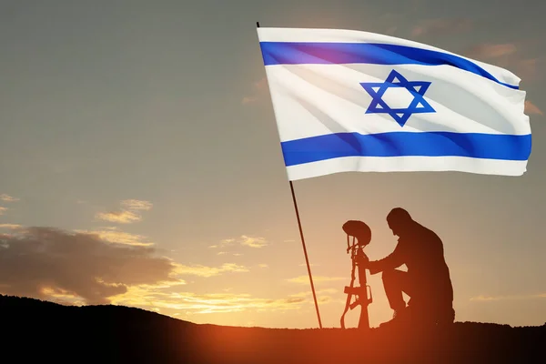 Silhouette of soldier kneeling with his head bowed with Israel flag against the sunrise in the desert. Concept - armed forces of Israel.