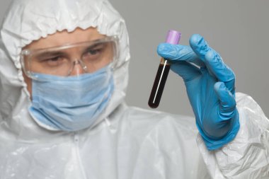 Scientific virologist. Biologist in protective suit and blue gloves holds test tube with blood. Test tube with viruses concept. Virus University employee.