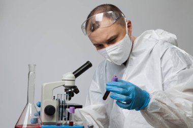 Bilimsel virolog. Koruyucu kıyafetli ve mavi eldivenli biyolog üzerinde kan olan test tüpü tutuyor. Virüs konseptli test tüpü. Virüs Üniversitesi çalışanı.