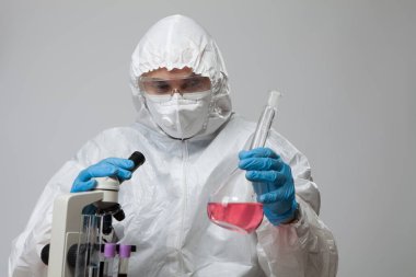 Scientific virologist. Biologist in protective suit and blue gloves holds flask with substance sample. Flask with viruses concept. Medicine and antidote in doctor hands. Virus University employee.