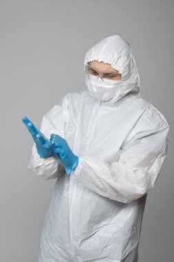 Scientific virologist. Biologist in protective suit and goggles putting on blue gloves. Viruses concept. Virus University employee.