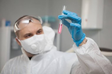 Scientific virologist. Biologist in protective suit and blue gloves holds test tube. Test tube with viruses concept. Medicine and antidote in doctor hands. Virus University employee.