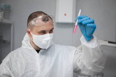 Scientific virologist. Biologist in protective suit and blue gloves holds test tube. Test tube with viruses concept. Medicine and antidote in doctor hands. Virus University employee.