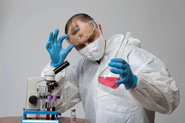 科学的ウイルス学者 保護スーツと青手袋の生物学者は 物質サンプルとフラスコを保持しています ウイルスの概念でフラスコ 医師の手で薬や解毒剤 ウイルス大学の従業員 — ストック写真