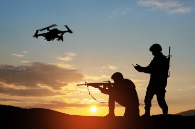 Silhouettes of soldiers are using drone and laptop computer for scouting during military operation against the backdrop of a sunset. Greeting card for Veterans Day, Memorial Day, Independence Day.