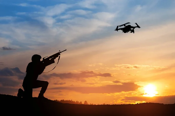 stock image Soldier trying to shoot down reconnaissance drone against the backdrop of a sunset. Soldier shoots a quadcopter. Modern methods of warfare. Technology concept.