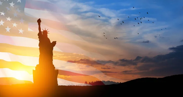 Statue of Liberty with a large american flag and sunset sky with flying birds on background. Greeting card for Independence Day. USA celebration.