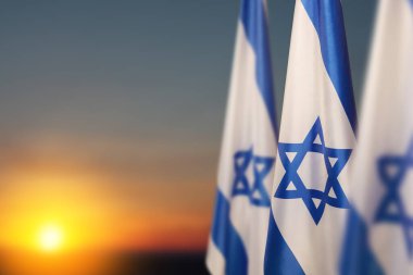 Israel flags with a star of David over cloudy sky background on sunset. Patriotic concept about Israel with national state symbols. Banner with place for text.