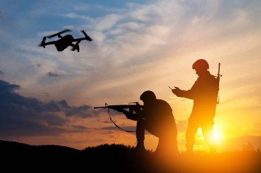 Silhouettes of soldiers are using drone and laptop computer for scouting during military operation against the backdrop of a sunset. Greeting card for Veterans Day, Memorial Day, Independence Day.