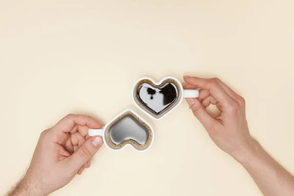 Woman and man hands holds heart shaped cup of coffee. Black hot coffee in a white heart-shaped cup.