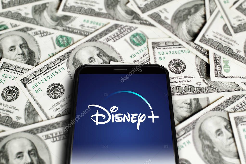 Disney Plus logo on smartphone screen on background of dollars. Dinsey plus is an American subscription video on-demand over-the-top streaming service. Moscow, Russia - November 1, 2022.