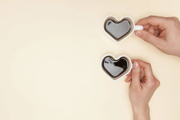 Woman and man hands holds heart shaped cup of coffee. Black hot coffee in a white heart-shaped cup.
