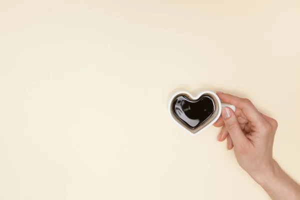 Woman hands holds heart shaped cup of coffee. Black hot coffee in a white heart-shaped cup.