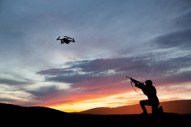 Asker, gün batımının arka planına karşı keşif uçağını düşürmeye çalışıyor. Asker bir kuadkopteri vuruyor. Modern savaş yöntemleri. Teknoloji konsepti.