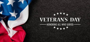 Closeup of American flag with Text Veterans Day Honoring All Who Served on black textured background. American holiday banner.