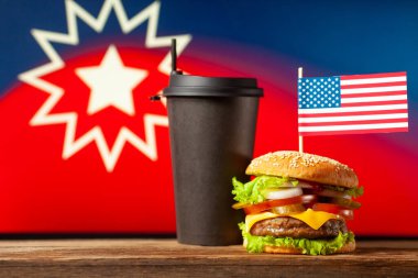 Üzerinde ABD bayrağı olan klasik Amerikan hamburgeri ve Junetenth sembol arka planında saman olan siyah kağıt bardak. Seçici odak ile yakın plan.