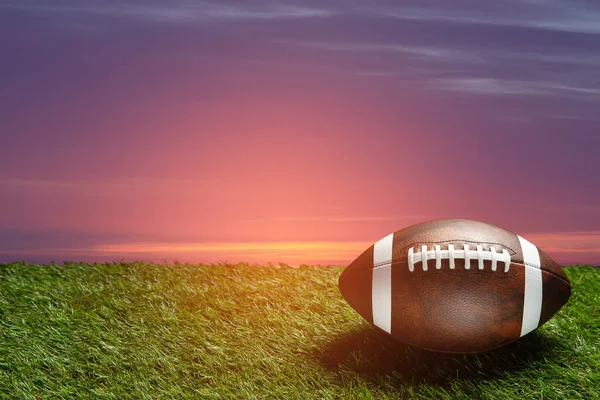American football ball on green grass field on background of sunset sky. Banner with space for text.