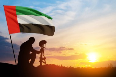 Silhouette of soldier kneeling with his head bowed against the sunrise or sunset and UAE flag. Concept of national holidays. Commemoration Day.