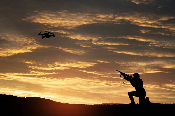 stock image Soldier trying to shoot down reconnaissance drone against the backdrop of a sunset. Soldier shoots a quadcopter. Modern methods of warfare. Technology concept.