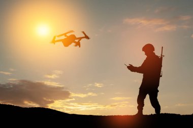 Silhouette of soldier are using drone and laptop computer for scouting during military operation against the backdrop of a sunset. Greeting card for Veterans Day, Memorial Day, Independence Day.