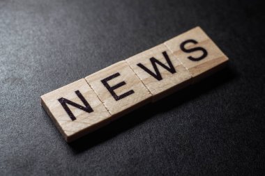 NEWS letter on wood block cubes on black background. Business communication concept.