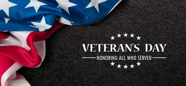 Closeup of American flag with Text Veterans Day Honoring All Who Served on black textured background. American holiday banner.