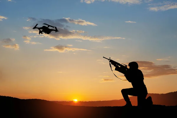 Soldier trying to shoot down reconnaissance drone against the backdrop of a sunset. Soldier shoots a quadcopter. Modern methods of warfare. Technology concept.