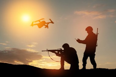 Silhouettes of soldiers are using drone and laptop computer for scouting during military operation against the backdrop of a sunset. Greeting card for Veterans Day, Memorial Day, Independence Day.