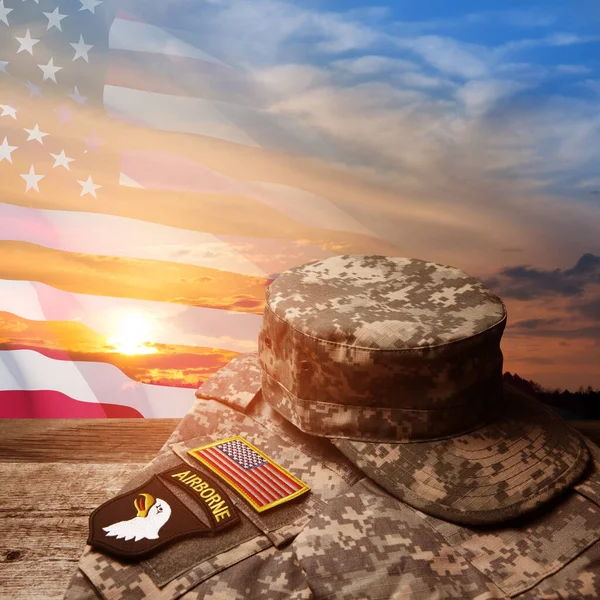 日没の空の背景にアメリカの国旗と古い木製のテーブルの上に記章とアメリカ軍の制服 記念日又は退役軍人の日の概念 — ストック写真