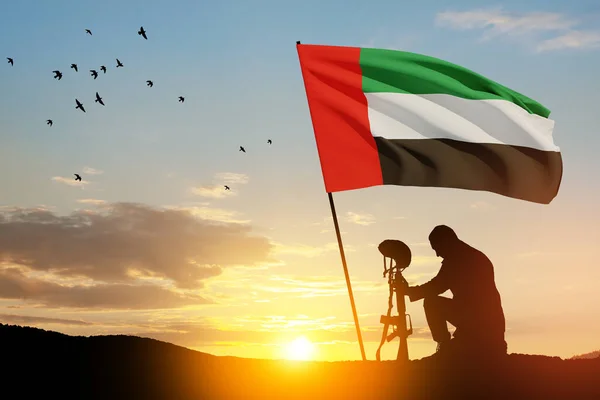 Silhouette of soldier kneeling with his head bowed against the sunrise or sunset and UAE flag. Concept of national holidays. Commemoration Day.