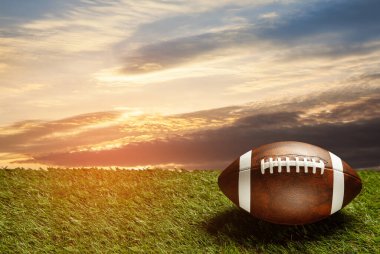 American football ball on green grass field on background of sunset sky. Banner with space for text.