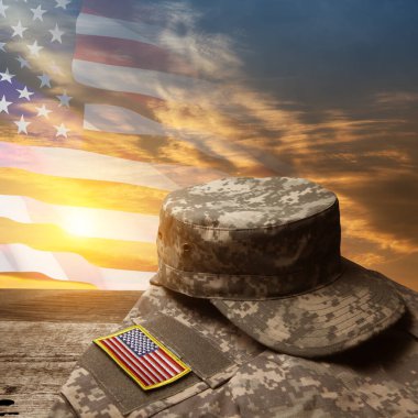 Amerikan askeri üniforması, üzerinde semboller olan eski ahşap bir masa, günbatımı gökyüzü arka planında Amerikan bayrağı. Anma Günü ya da Gaziler Günü konsepti.