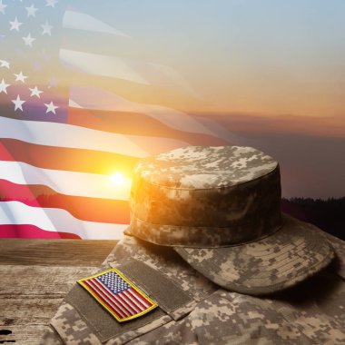 Amerikan askeri üniforması, üzerinde semboller olan eski ahşap bir masa, günbatımı gökyüzü arka planında Amerikan bayrağı. Anma Günü ya da Gaziler Günü konsepti.