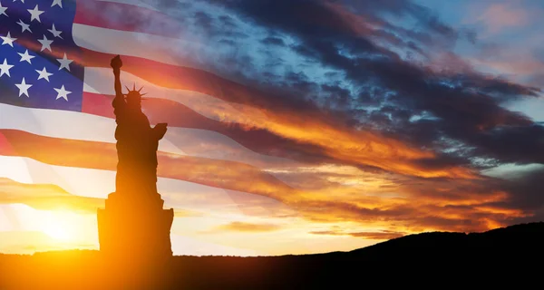 stock image Statue of Liberty with a large american flag and sunset sky on background. Greeting card for Independence Day. USA celebration.