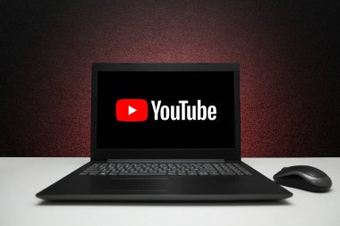 YouTube logosu ekrandaki dizüstü bilgisayarda, fareyle birlikte siyah desenli duvarda kırmızı ışık var. Astana, Kazakistan - 23 Mart 2023.