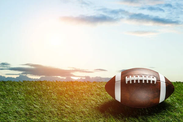 American football ball on green grass field on background of blue sky. Banner with space for text.