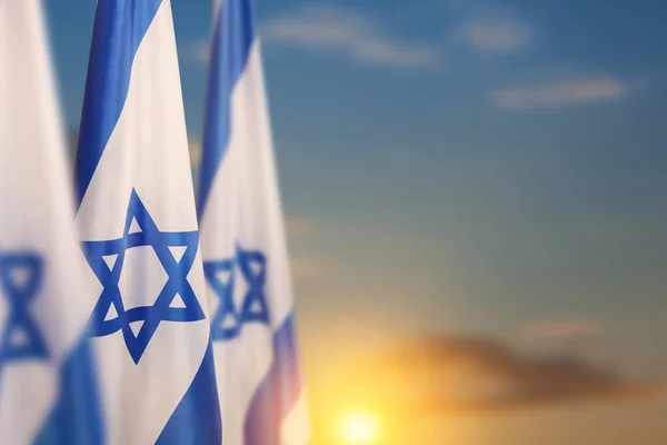 Israel flags with a star of David over cloudy sky background on sunset. Patriotic concept about Israel with national state symbols. Banner with place for text.