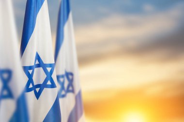Israel flags with a star of David over cloudy sky background on sunset. Patriotic concept about Israel with national state symbols. Banner with place for text.