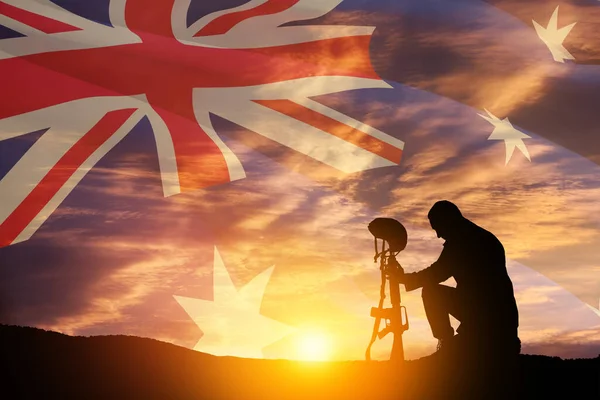 Silhouette of soldier kneeling with his head bowed against the sunrise or sunset and Australia flag. Anzac Day. Remembrance Day.